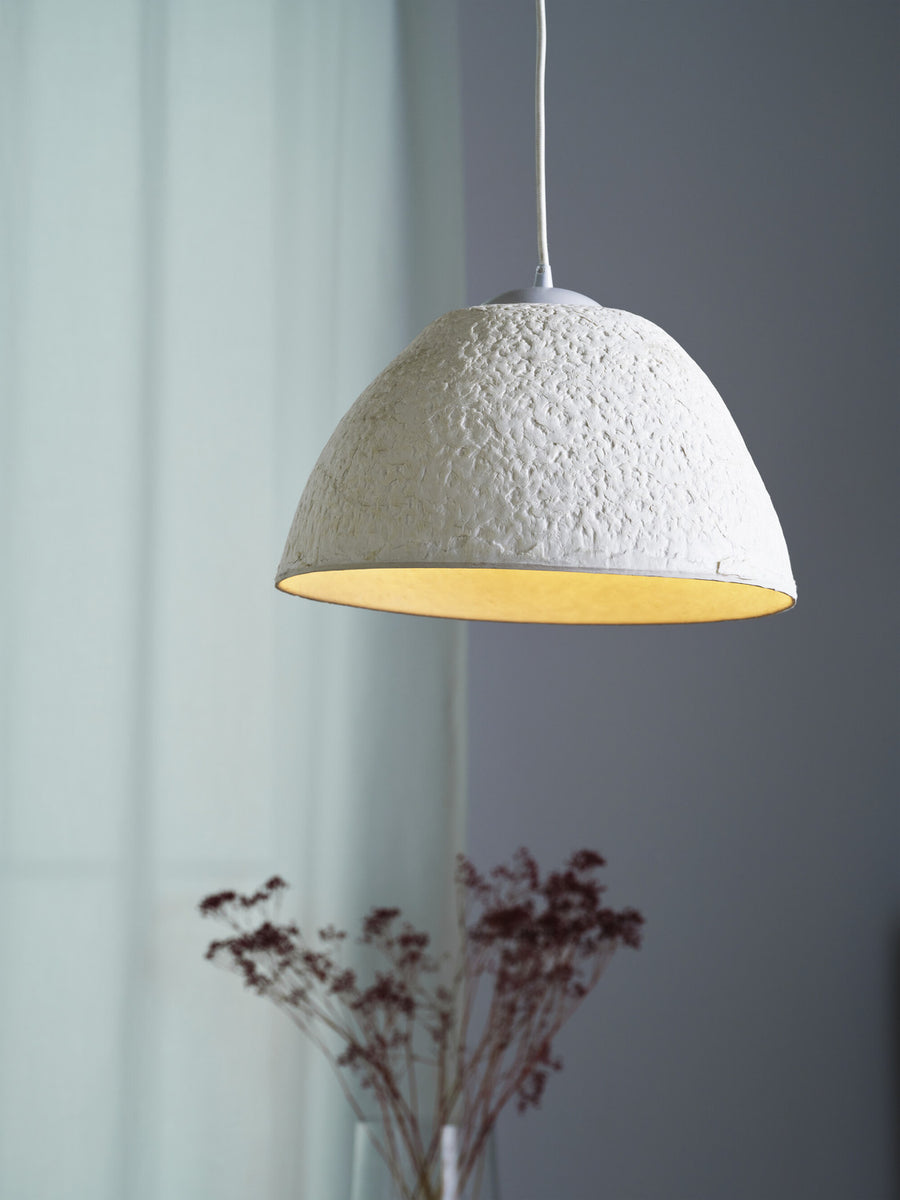 Détail de l'abat-jour blanc texturé, lumière chaude à l'intérieur, fleurs séchées floues.
