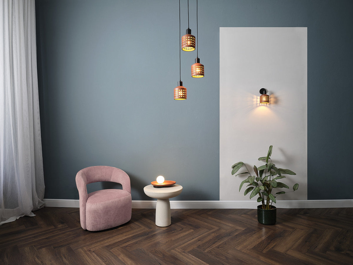 Mise en ambiance salon avec suspensions allumées, fauteuil rose et plante.
