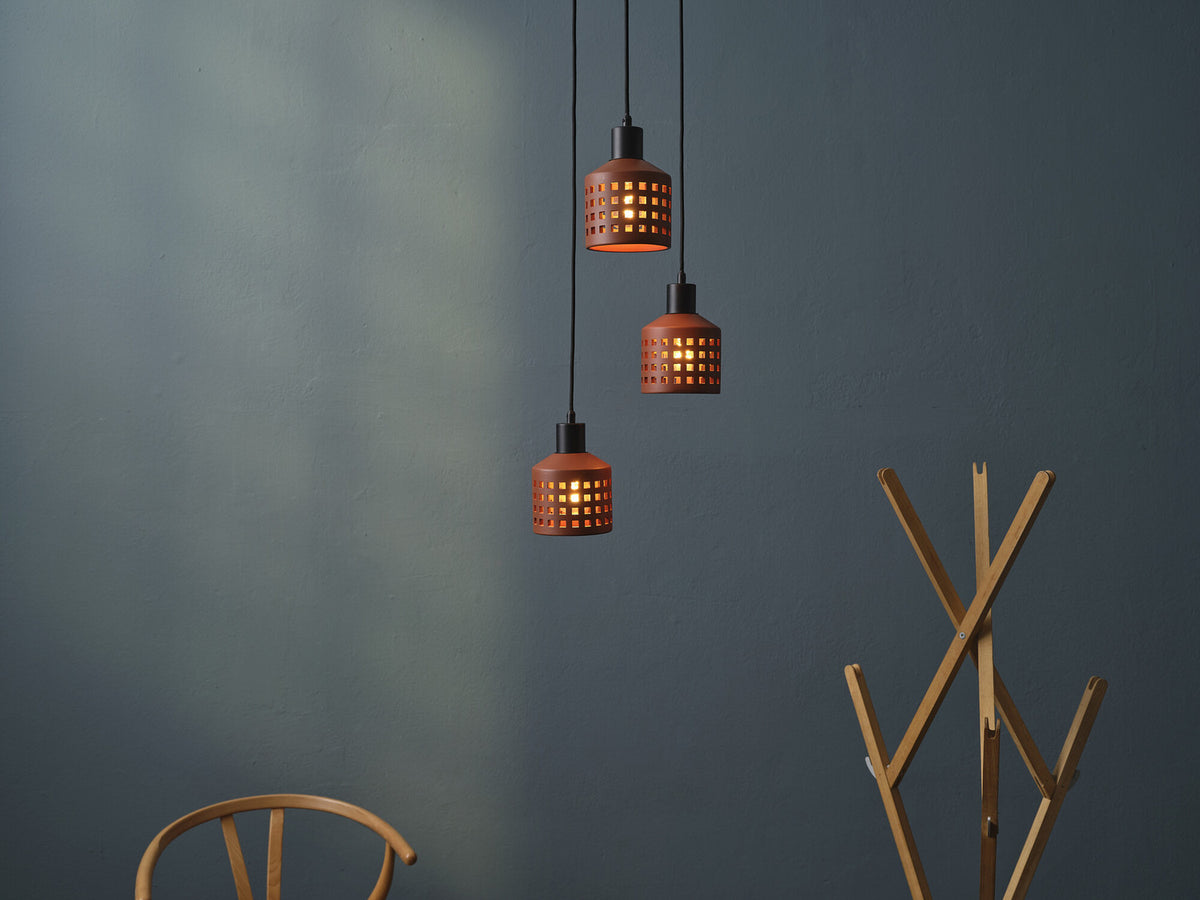 Trois suspensions en terre cuite allumées devant un mur gris et portemanteau.
