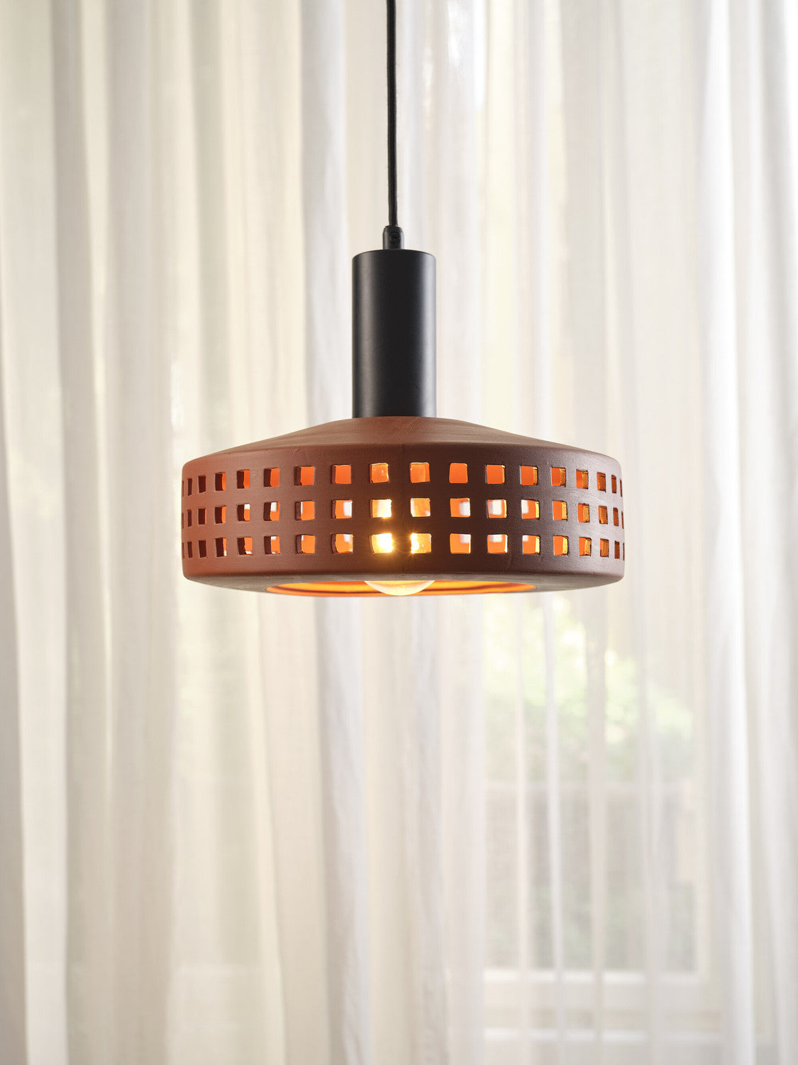Gros plan du luminaire allumé devant un rideau blanc translucide.