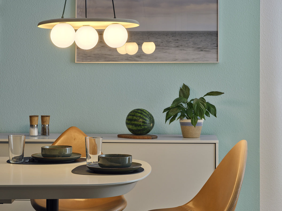 Suspension allumée au-dessus d'une table à manger dans une pièce bleu-vert.