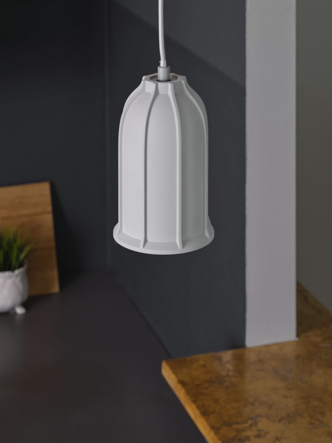 Détail d'une suspension grise moderne accrochée au-dessus d'un comptoir sombre.