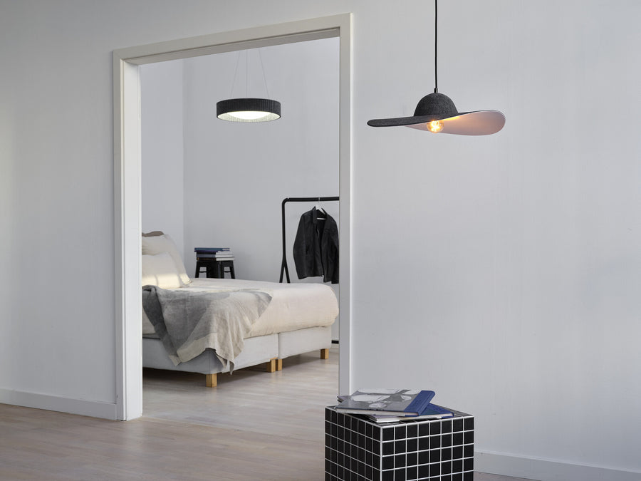Vue à travers une porte : suspension en feutre au loin et autre luminaire au premier plan.