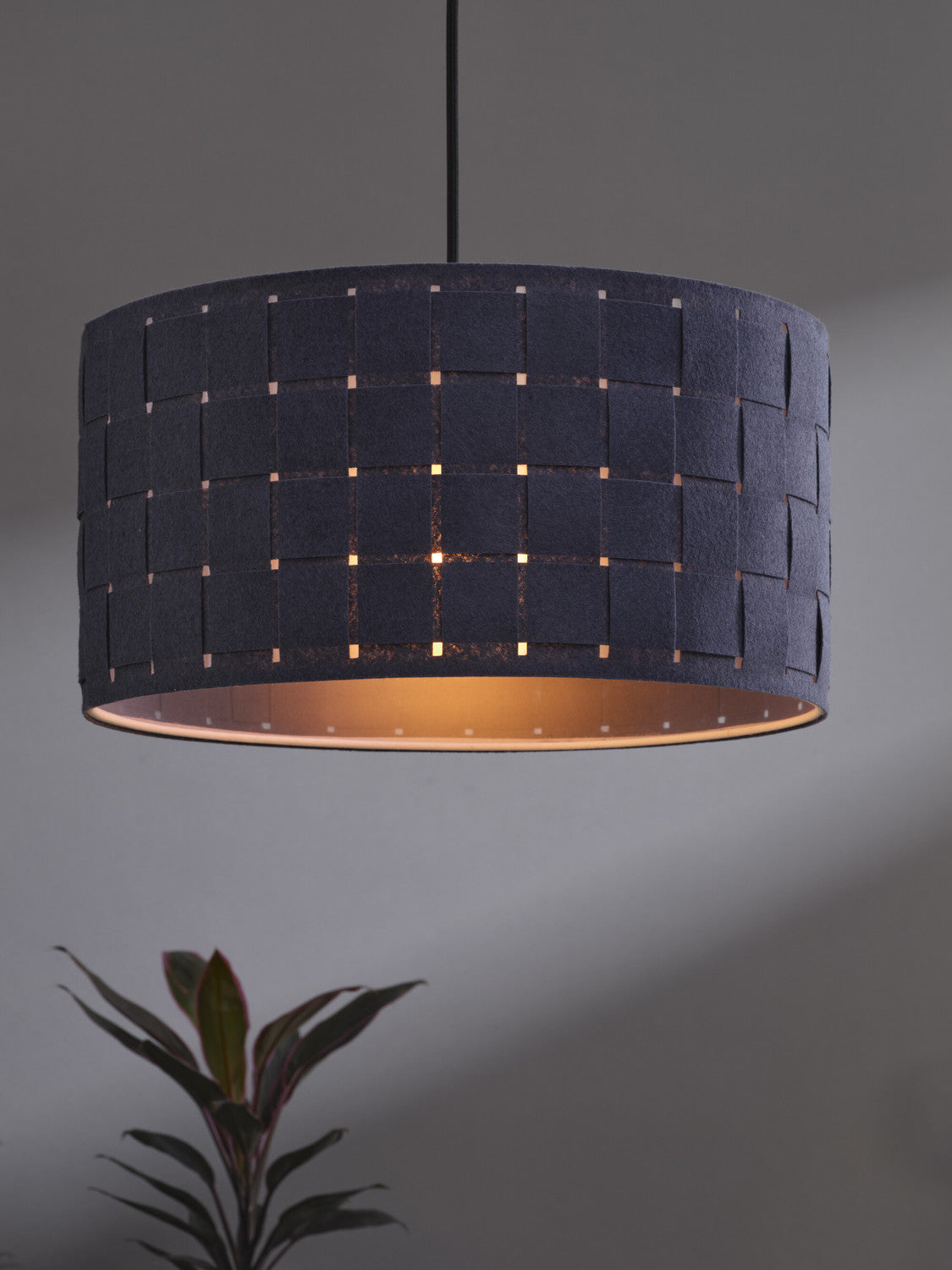 Détail de l'abat-jour allumé révélant le motif tressé et la lumière chaude.