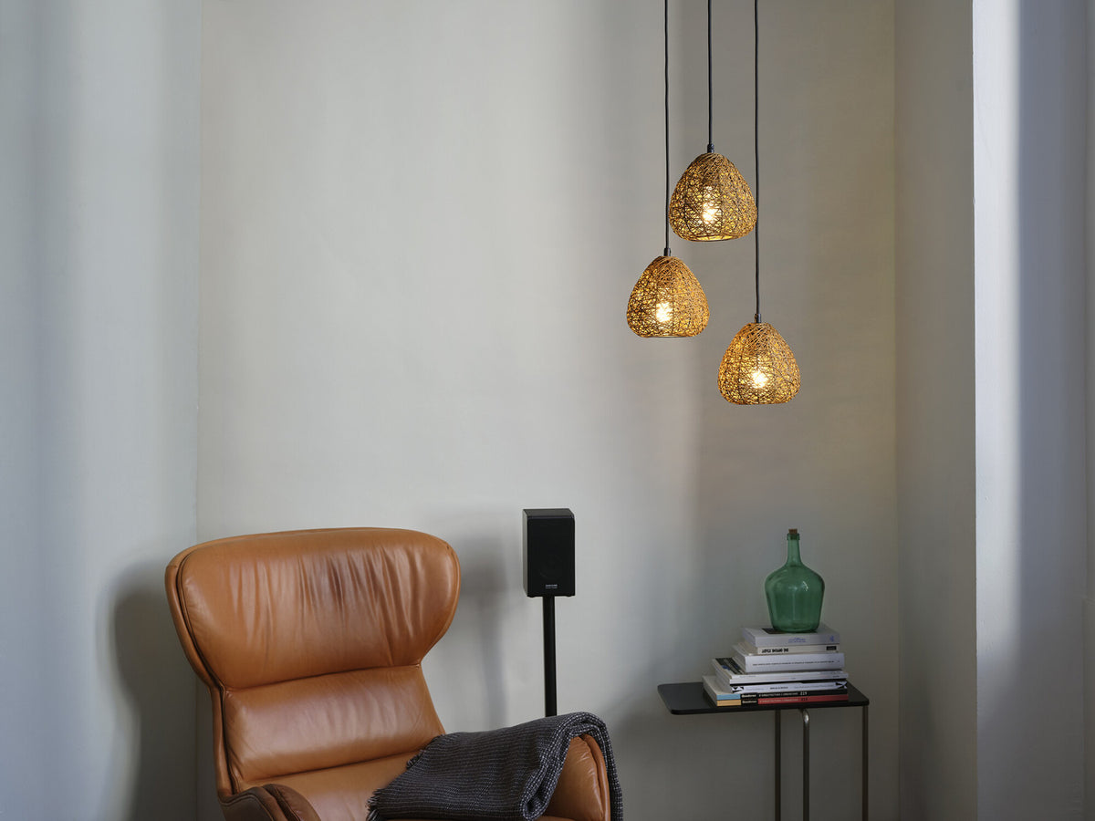 Mise en ambiance salon, suspensions allumées au-dessus d’un fauteuil en cuir camel.