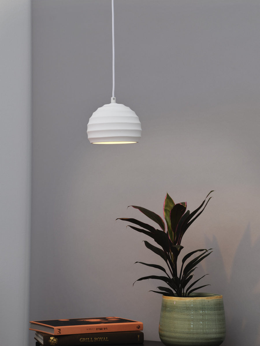 Suspension blanche allumée au-dessus de livres et d'une plante verte, sur fond gris.