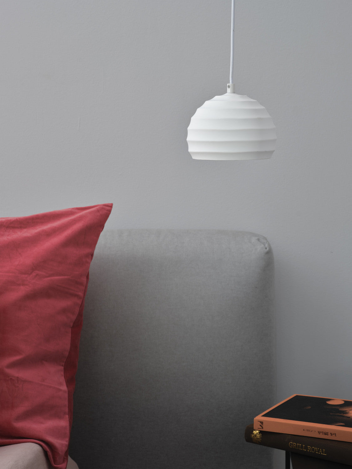 Gros plan sur la suspension blanche striée, près d'un coussin rose et d'un livre.
