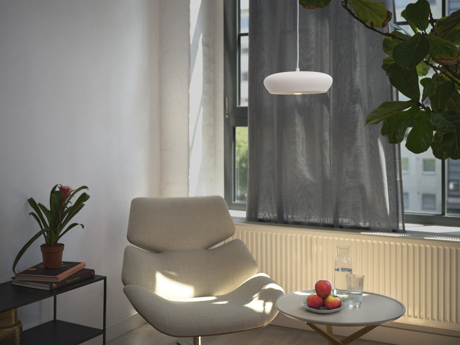 Suspension blanche dans un salon lumineux, près d’une fenêtre et d’un fauteuil beige.