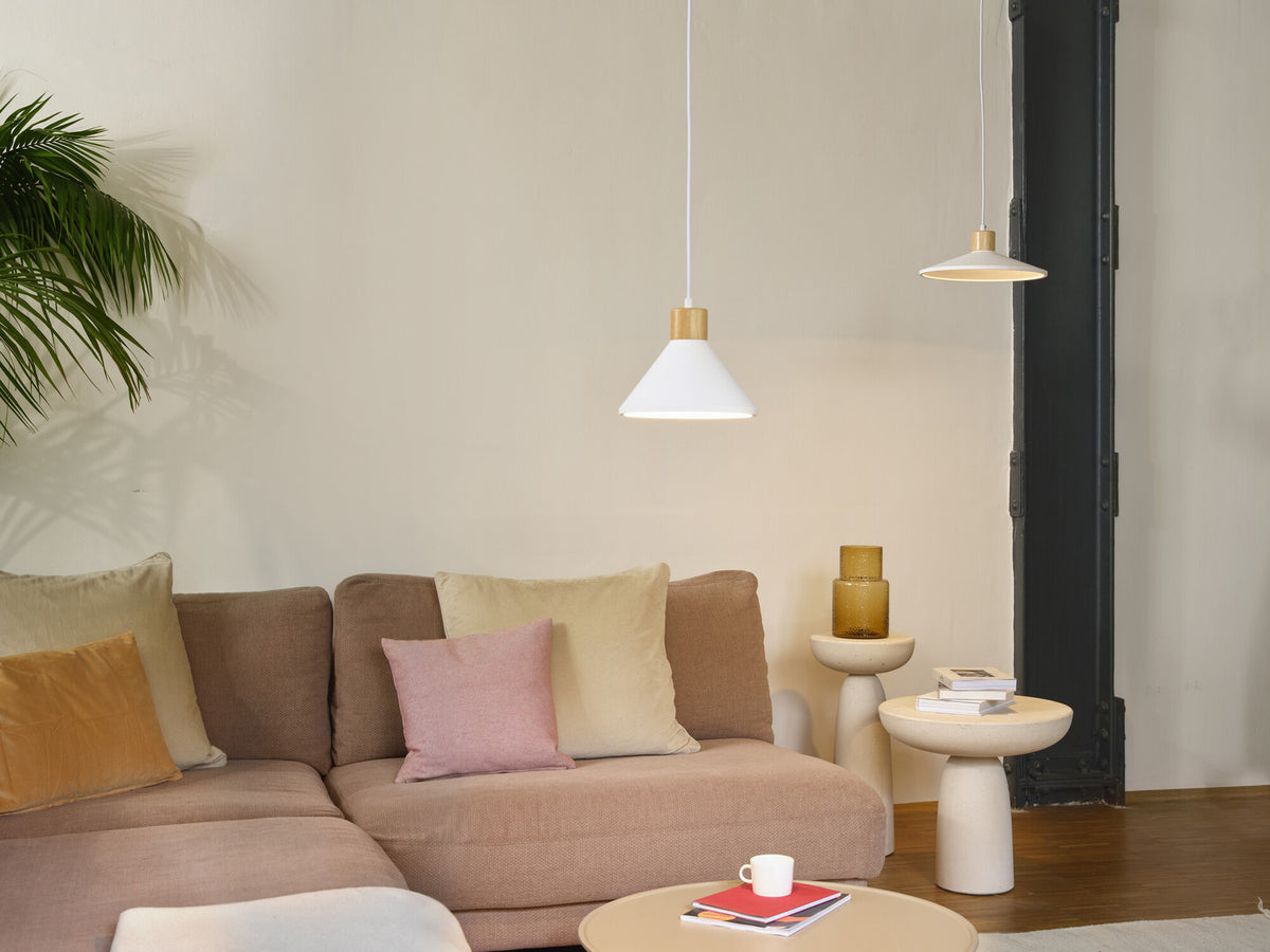 Deux suspensions blanches au-dessus d’un salon, canapé rose, coussins et plante verte.