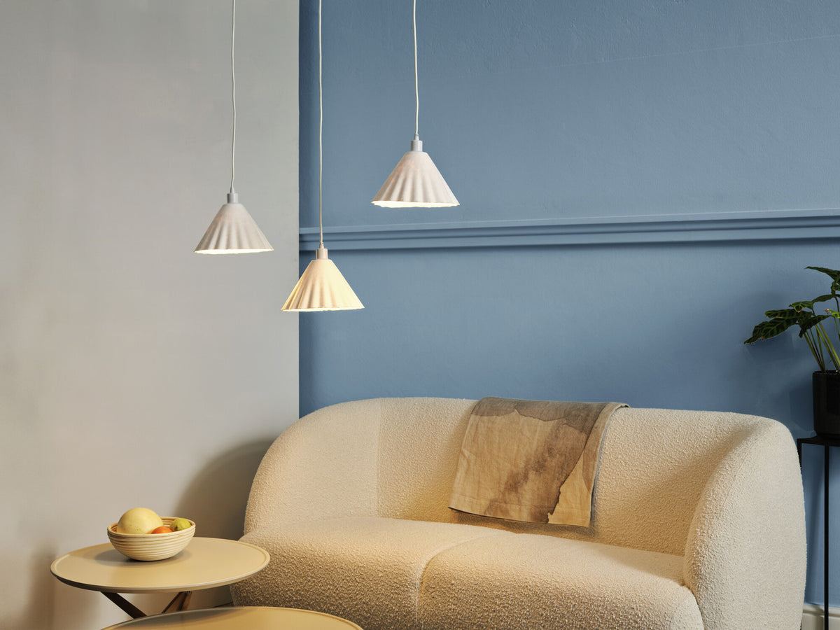 Mise en ambiance : trois suspensions éclairent un canapé beige devant un mur bleu.