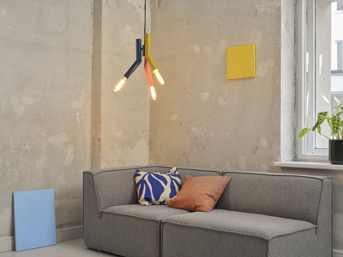 Mise en ambiance dans un salon, suspension multicolore allumée au-dessus d’un canapé gris.