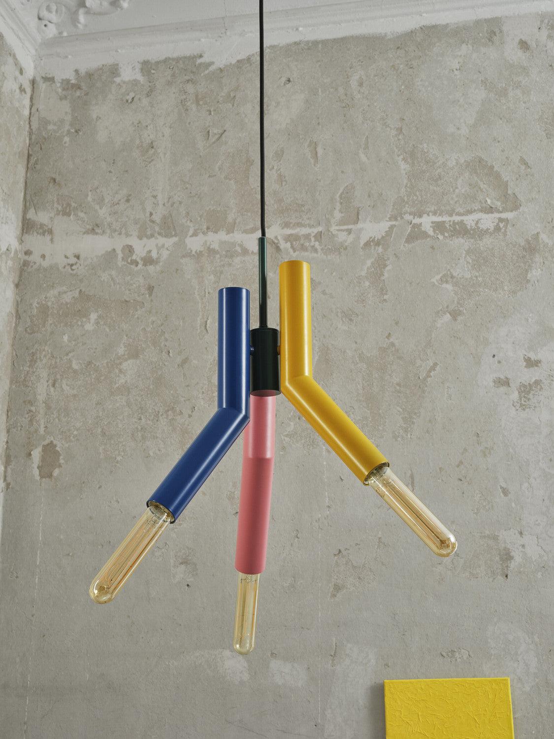 Vue en contre-plongée de la suspension colorée sous un plafond mouluré, mur béton en fond.