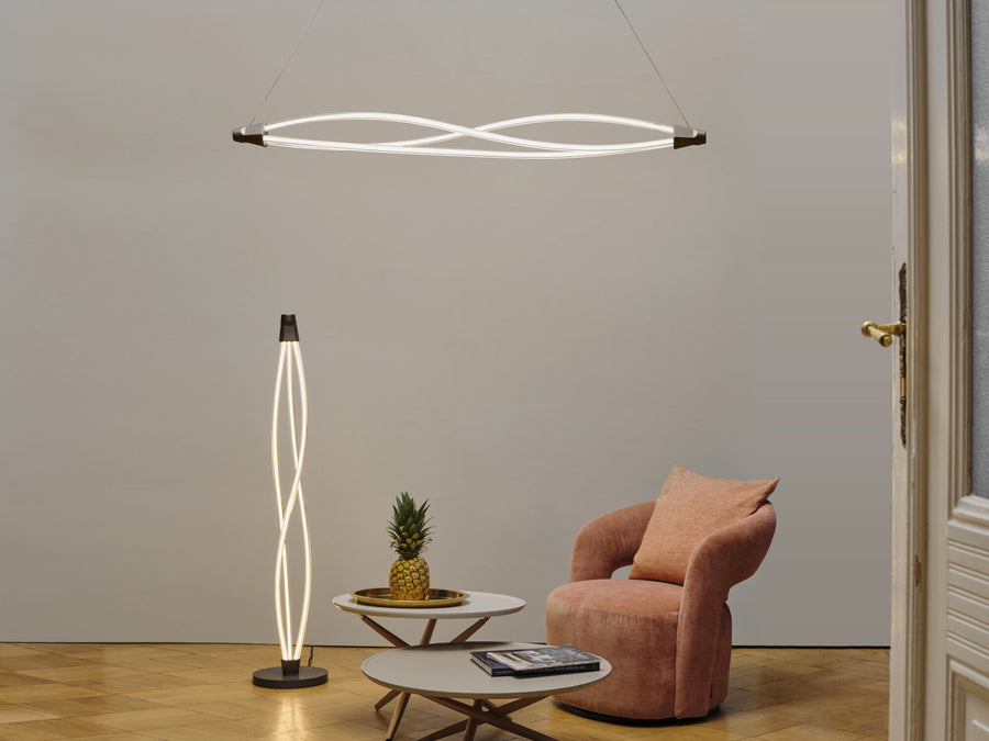 Suspension et lampe sur pied torsadées allumées dans un salon avec fauteuil rose.