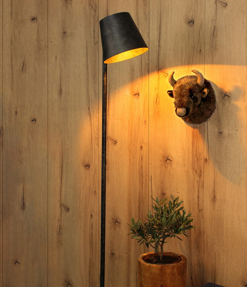 Lampadaire allumé devant un mur de bois, tête de bison et plante en pot