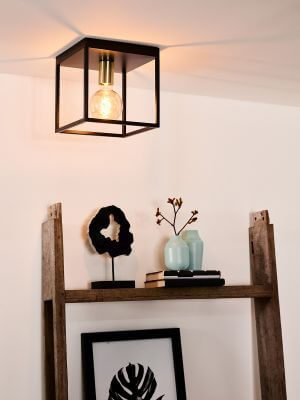 Plafonnier cubique noir et doré allumé au plafond dans une pièce avec étagère en bois.