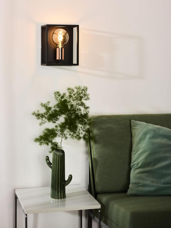 Applique murale allumée fixée sur un mur blanc au-dessus d'une table et d'un canapé vert