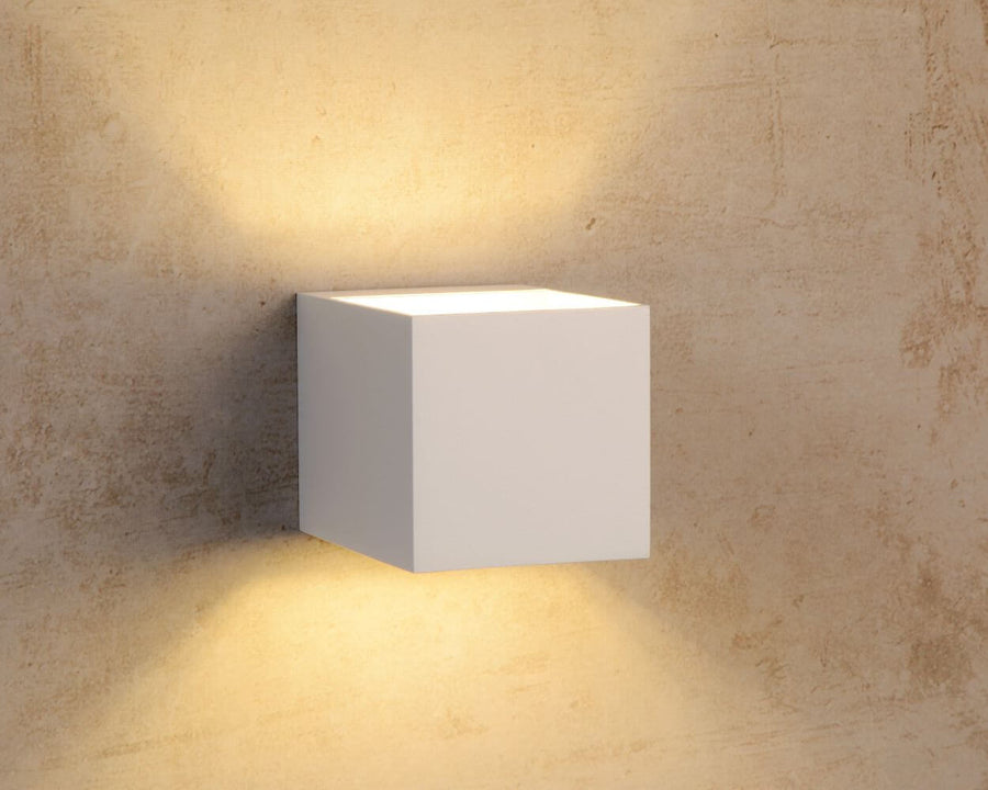 Applique cubique blanche allumée sur un mur beige texturé, lumière diffusée en haut et en bas.
