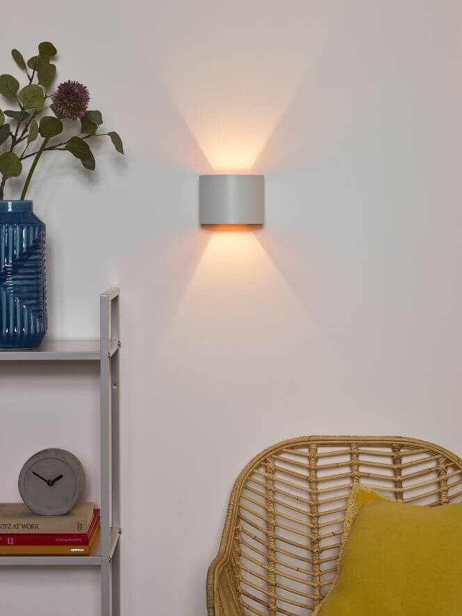 Vue rapprochée de l'applique blanche éclairant le mur, vase bleu et coussin