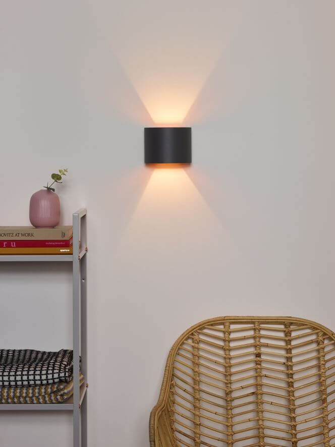 Mise en situation de l'applique grise dans un intérieur avec étagère et fauteuil rotin