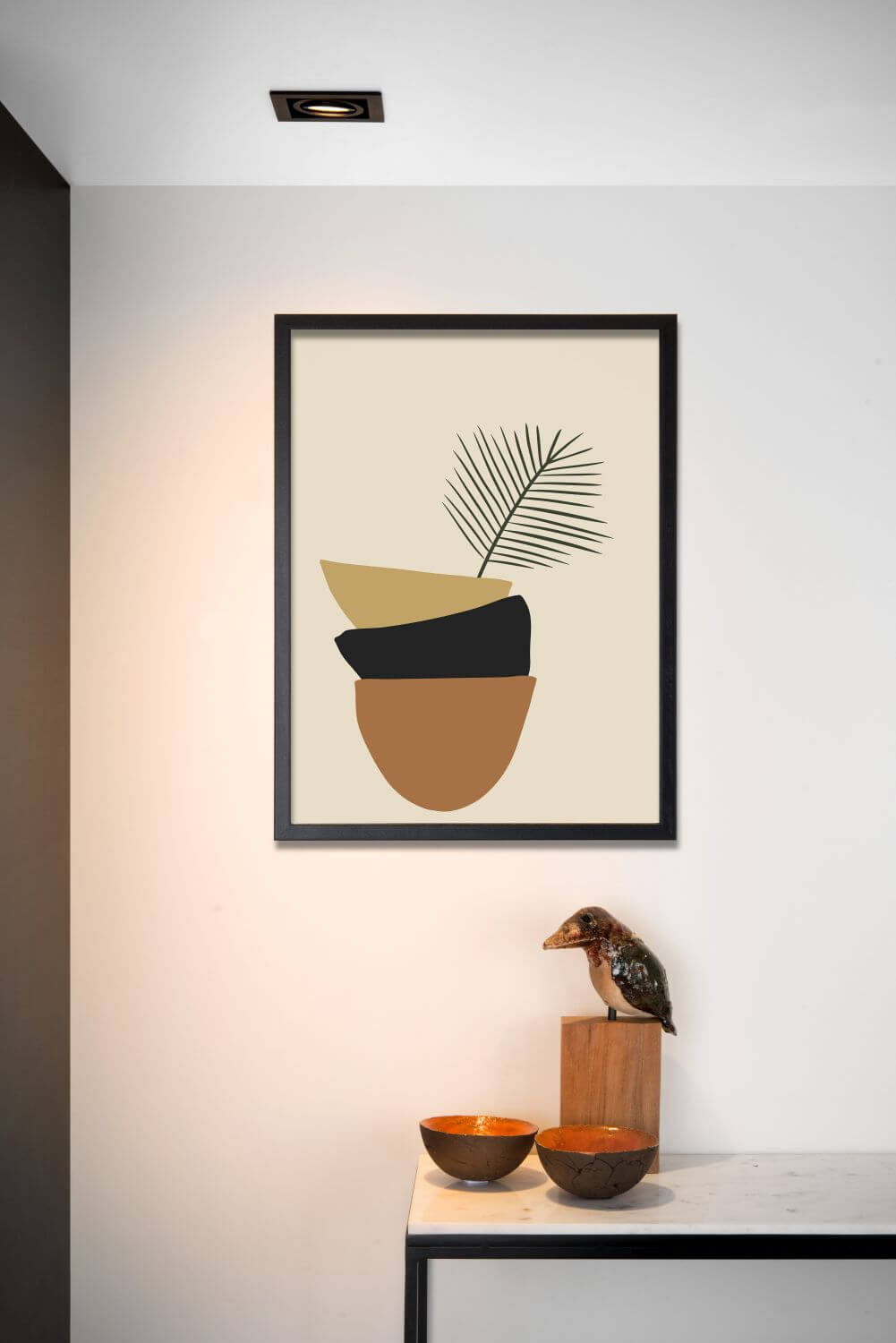 Spot encastré noir au plafond éclairant une affiche encadrée et une console décorée