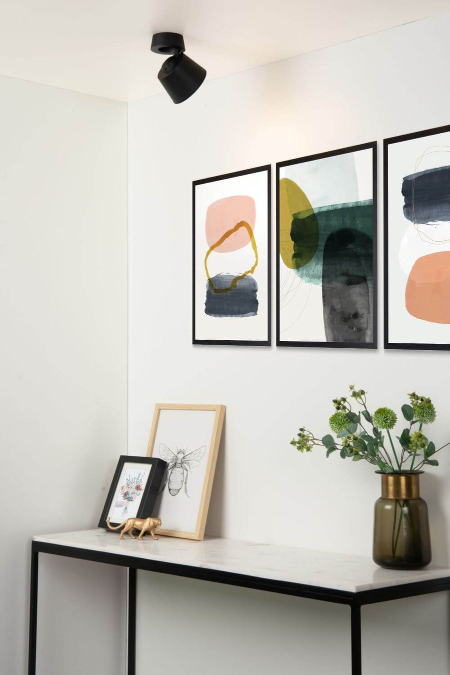 Plafonnier noir monté au plafond, orienté vers un mur orné de trois cadres.