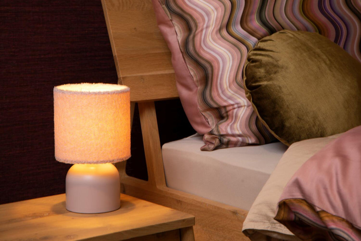 Autre vue de la lampe rose allumée près du lit et des coussins