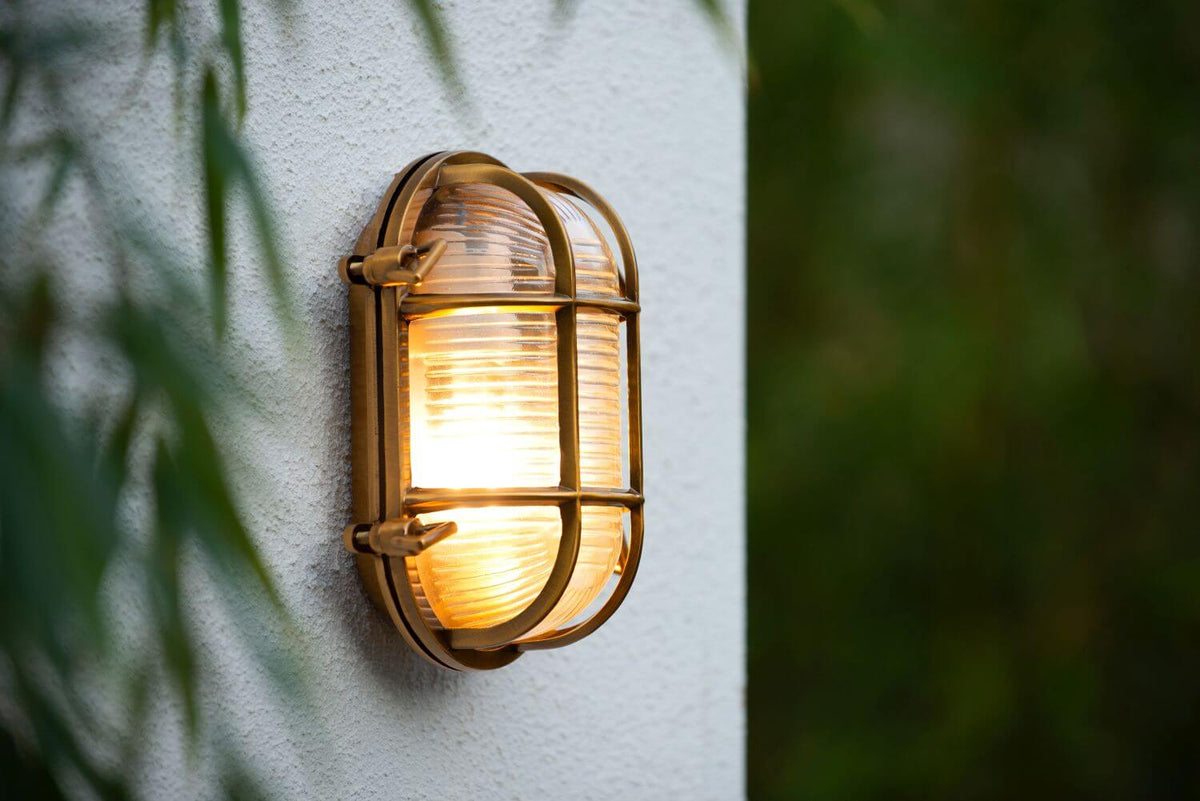 Gros plan sur l'applique dorée allumée, verre strié et grille métallique visibles.