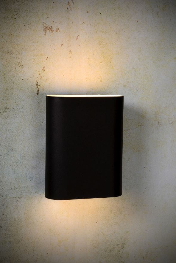 Applique noire allumée diffusant une lumière chaude sur un mur texturé beige.