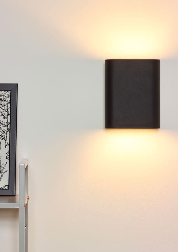 Mise en ambiance de l'applique murale noire éclairant un mur clair.