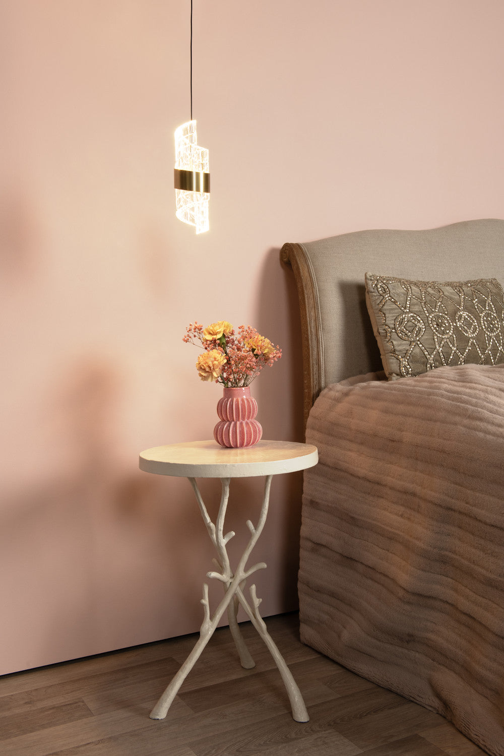 Vue en situation du luminaire suspendu, éclairant une chambre avec lit et table d'appoint.