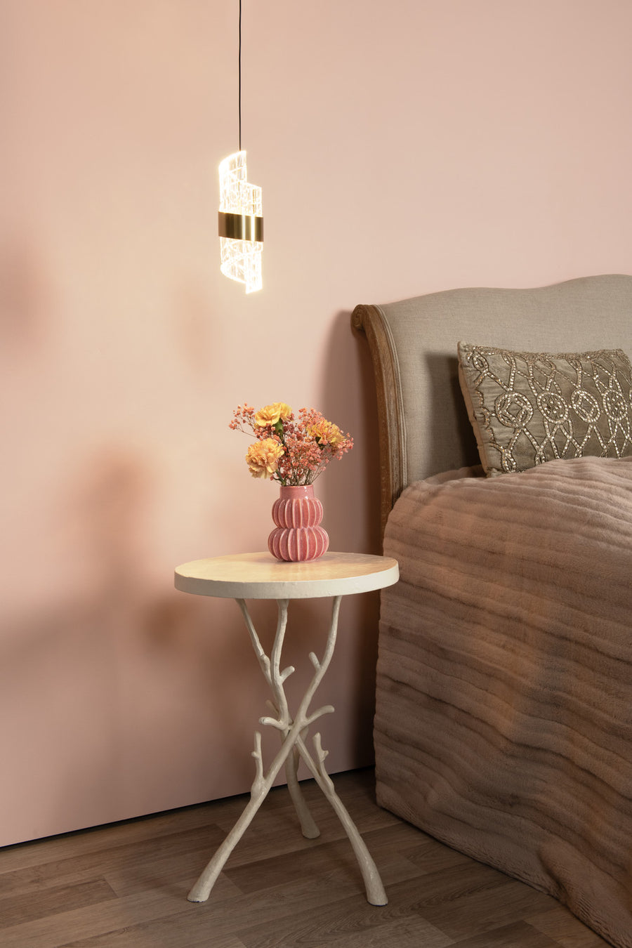 Vue en situation du luminaire suspendu, éclairant une chambre avec lit et table d'appoint.