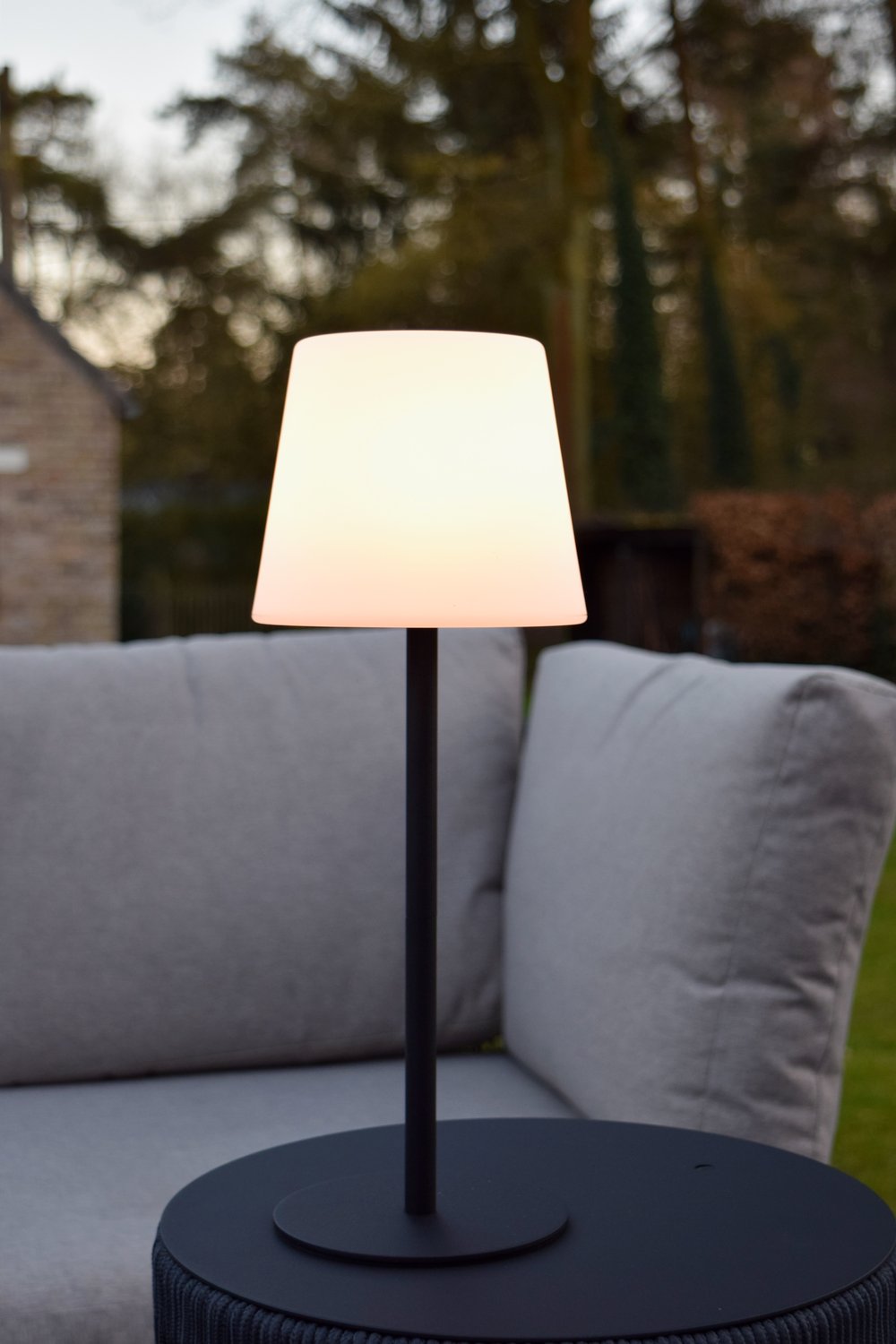 Mise en ambiance extérieure, lampe posée sur table basse devant canapé de jardin