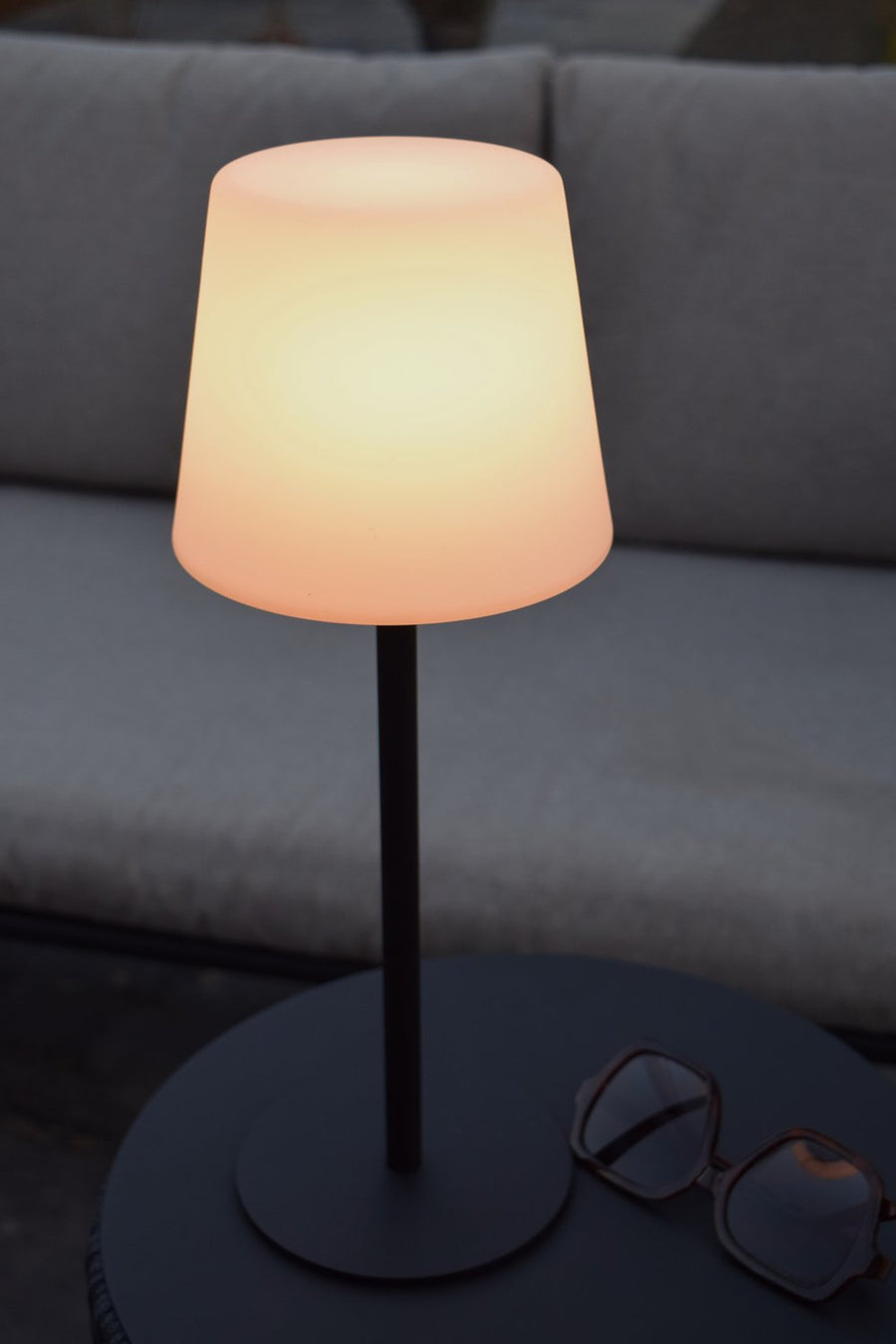 Lampe allumée sur table ronde sombre avec lunettes de soleil à côté