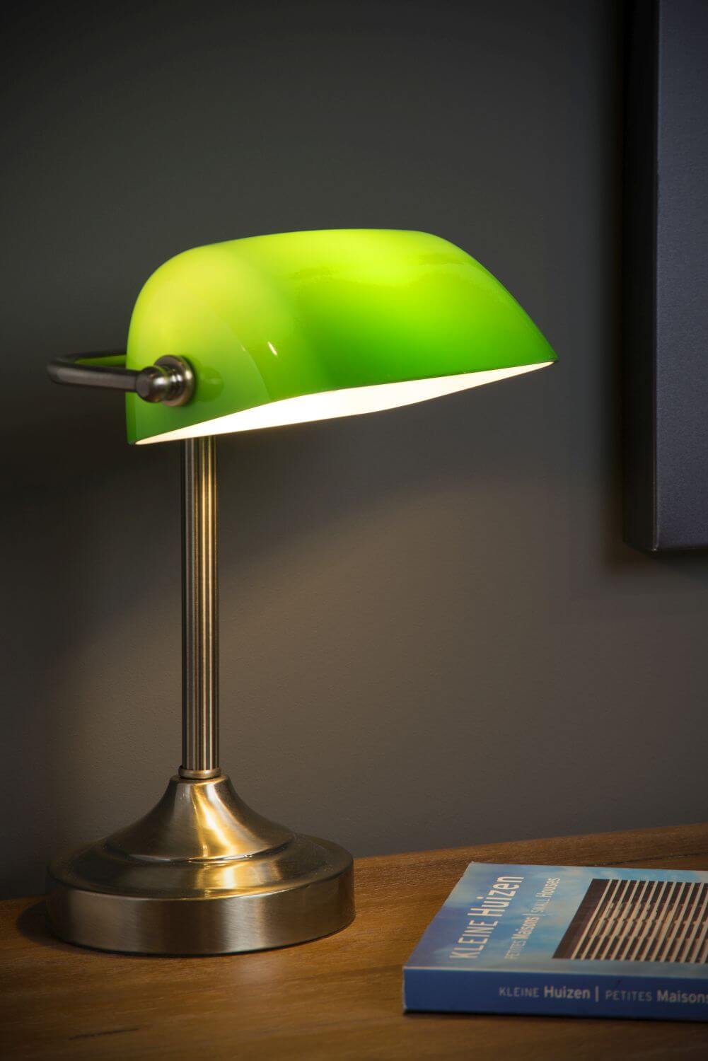 Lampe allumée posée sur un bureau en bois, près d’un livre, dans une ambiance sombre.