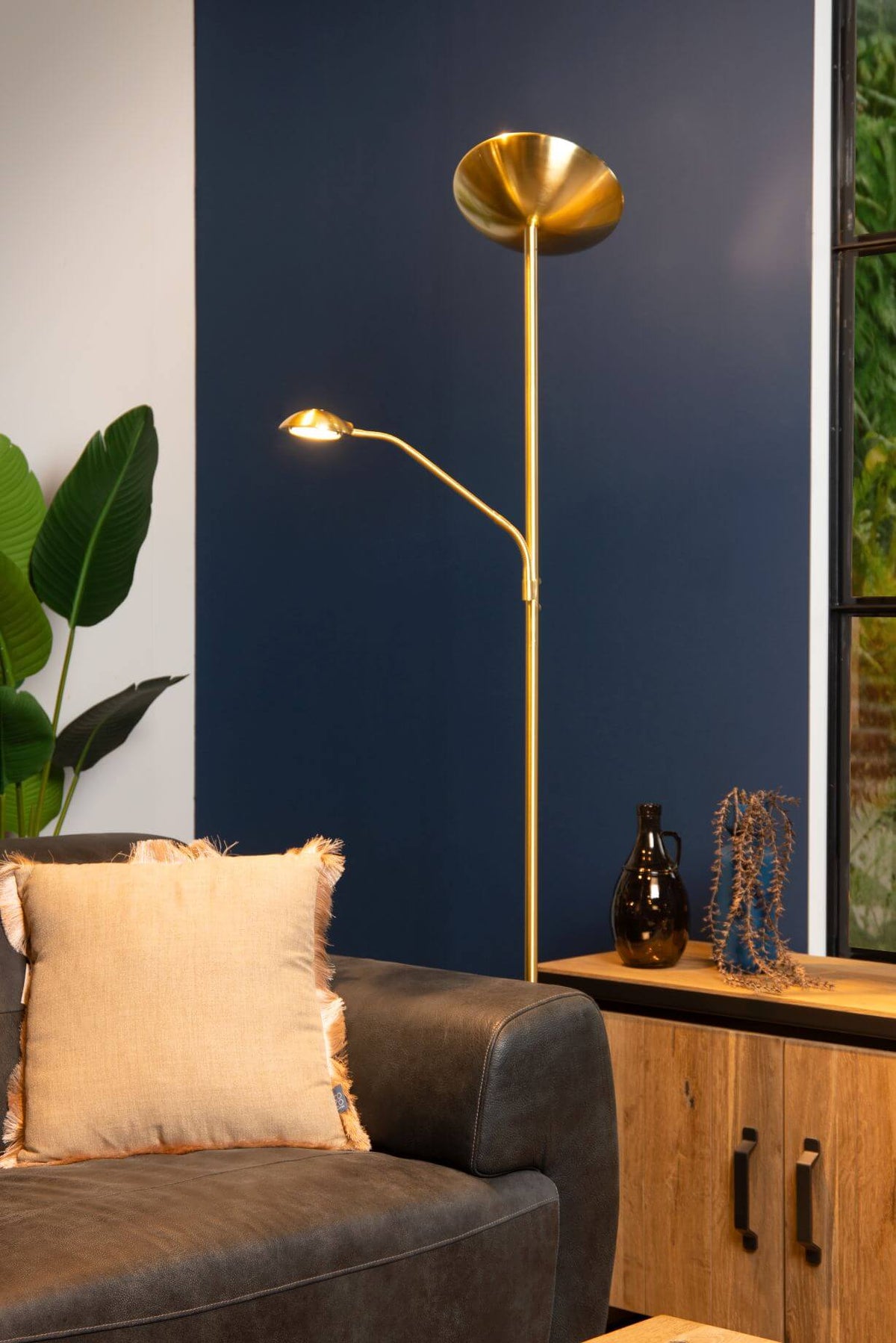 Mise en ambiance du lampadaire doré devant un mur bleu nuit et une plante