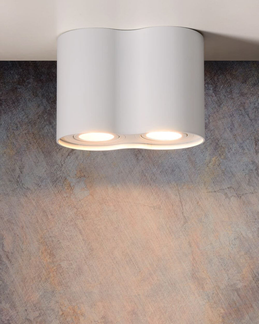 Plafonnier blanc allumé, projetant deux halos lumineux sur un mur texturé sombre.