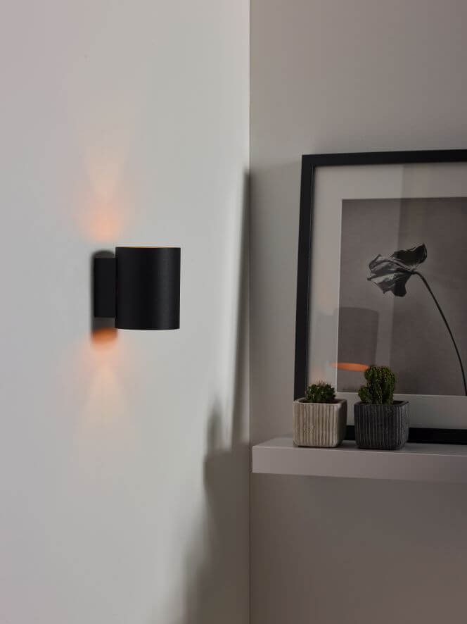 Vue rapprochée de l'applique noire allumée, halo orangé projeté sur le mur