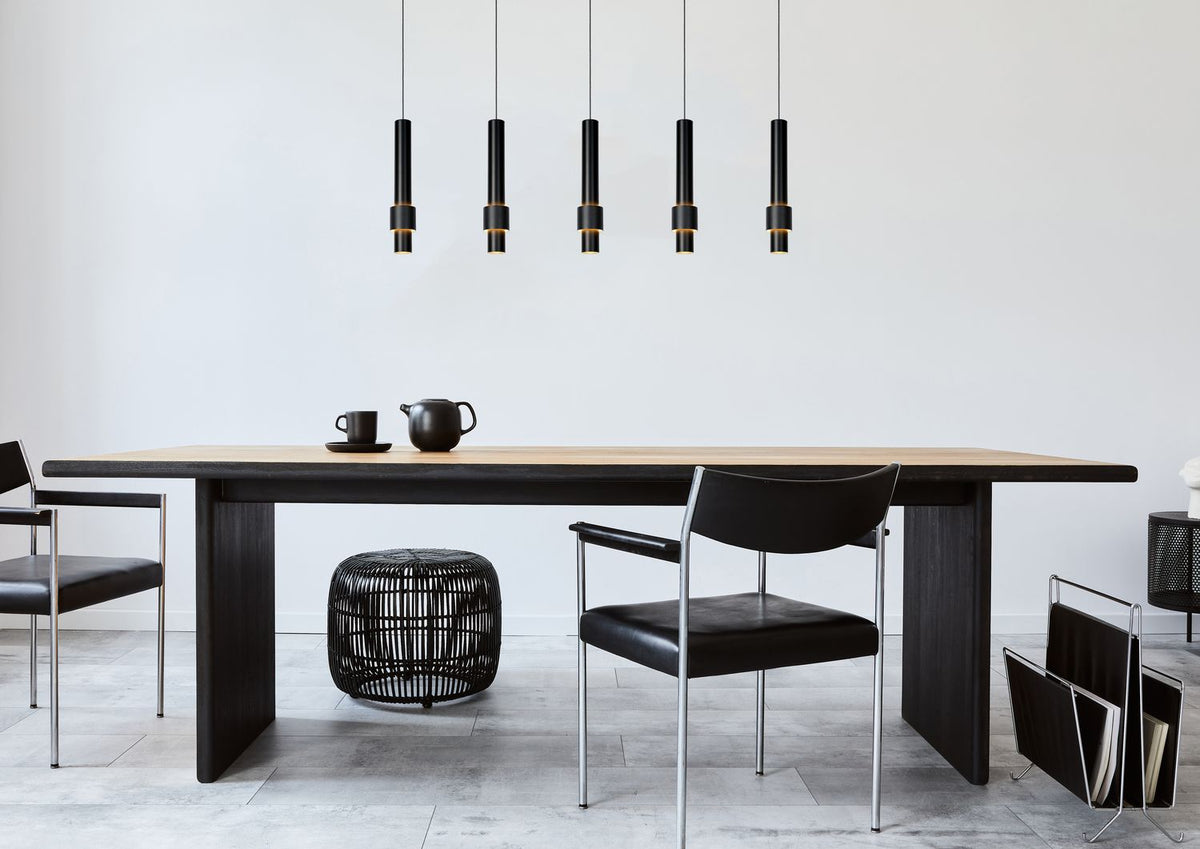 Mise en ambiance avec longue table en bois clair, chaises noires et tabouret tressé