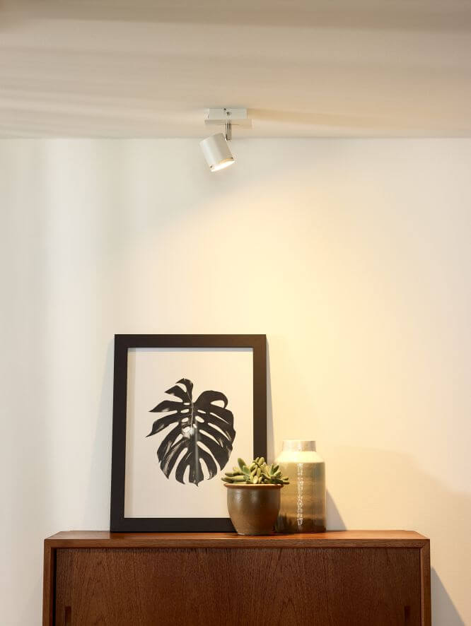 Spot plafonnier blanc orientable éclairant un mur au-dessus d'un meuble en bois