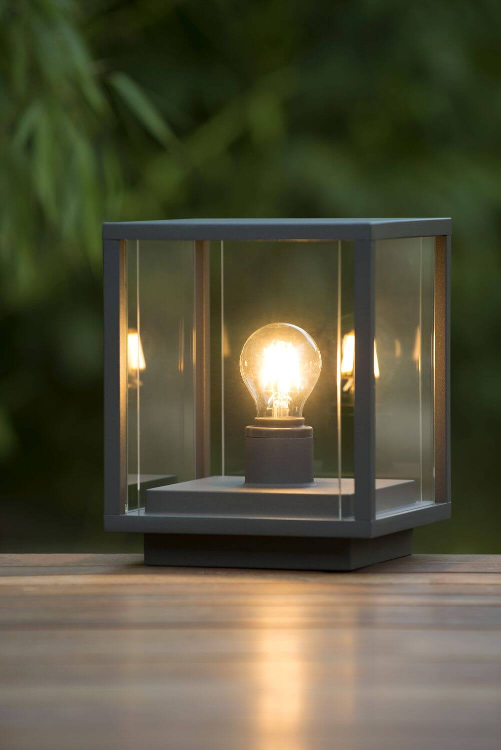 Vue rapprochée du luminaire cubique allumé posé sur une surface en bois, reflets visibles.