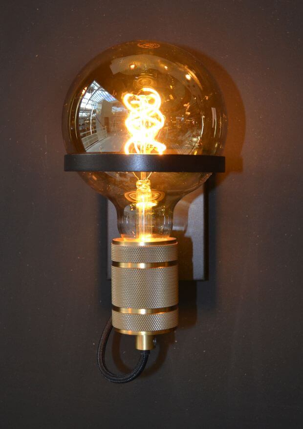 Vue rapprochée du luminaire mural montrant le culot doré moleté et l'ampoule allumée