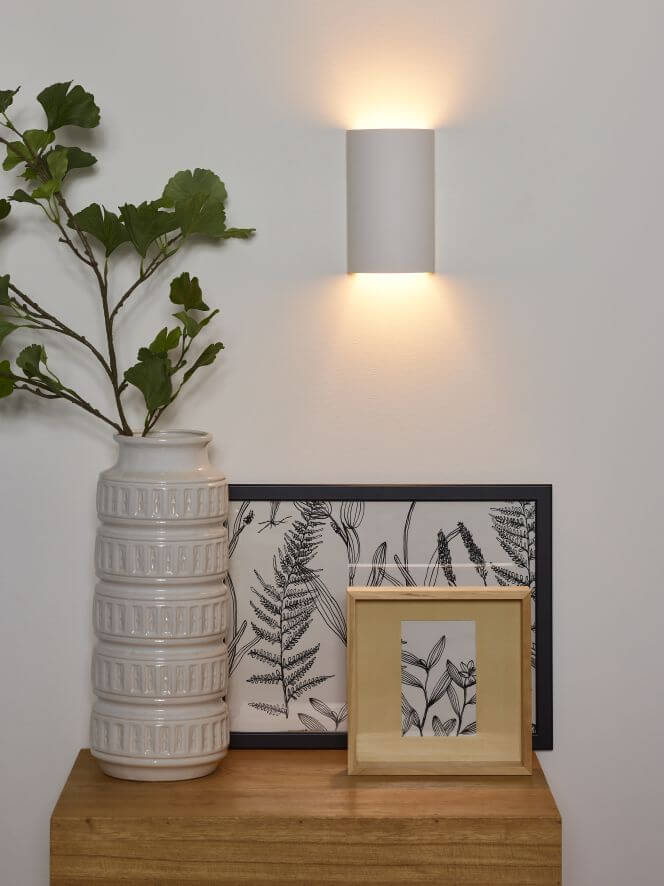 Vue rapprochée de l'applique murale allumée, vase et cadre sur commode