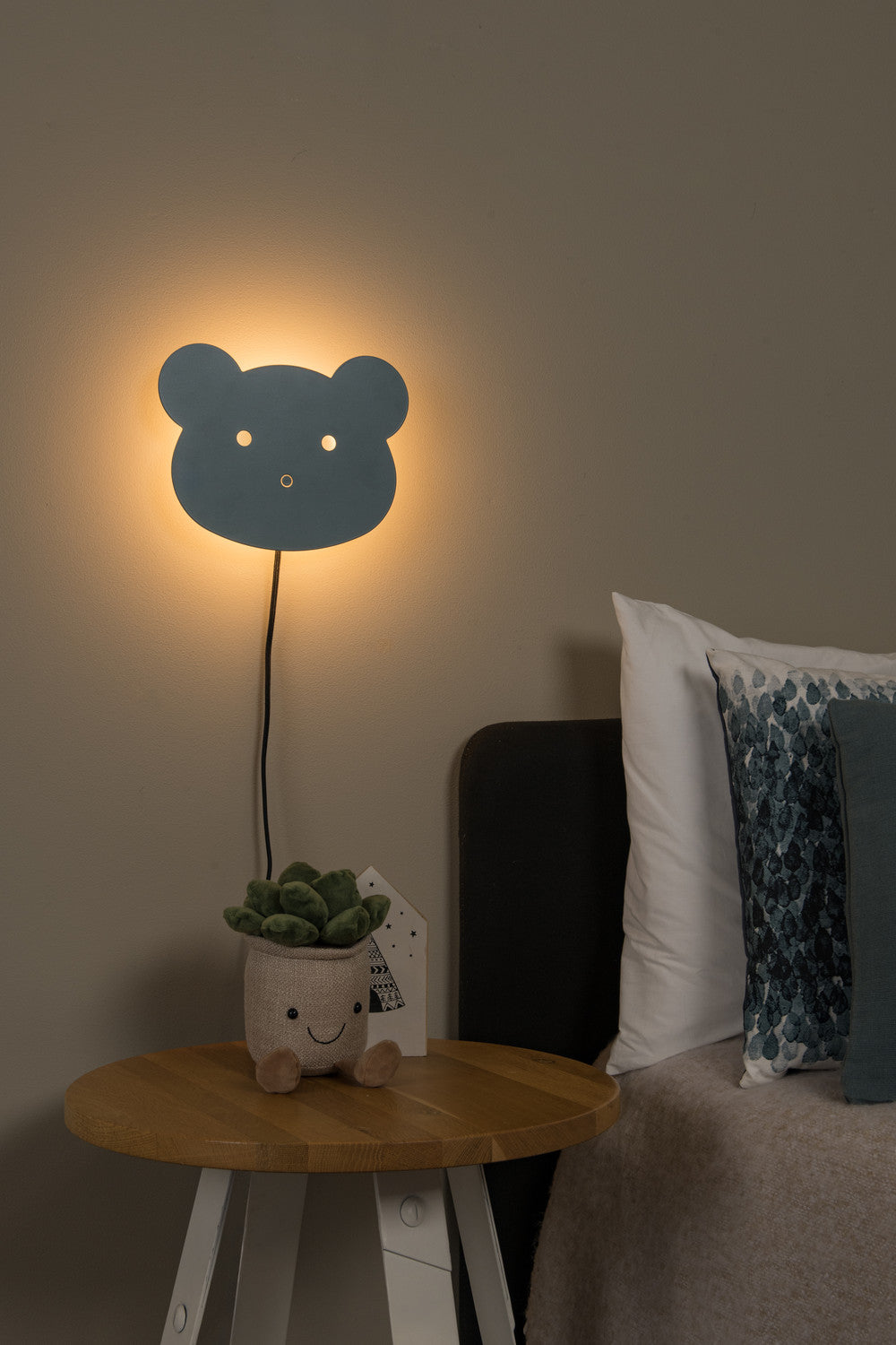 Vue avec applique murale tête d'ours bleue allumée au-dessus de la table de nuit.
