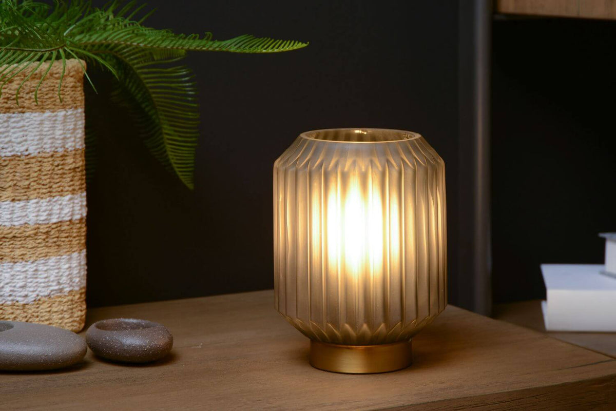 Gros plan de la lampe à poser allumée, posée sur un meuble en bois foncé.
