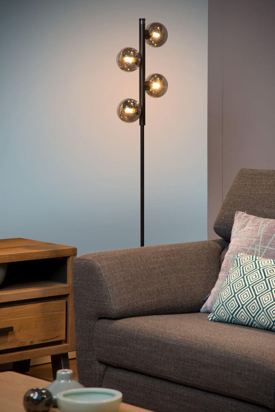 Lampadaire design en situation, près d'un canapé gris et d'une table basse en bois.