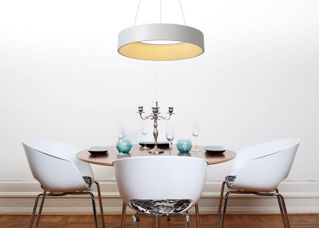 Suspension ronde blanche au-dessus d'une table avec trois chaises, bougeoirs et verres