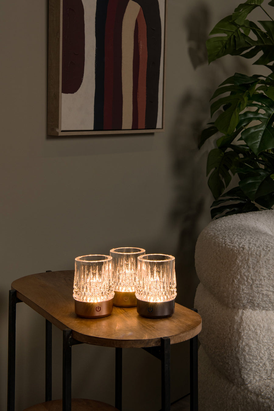 Trois lampes à poser cuivrées allumées sur une table basse en bois, décor intérieur chaleureux.