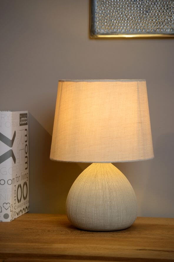 Vue rapprochée de la lampe beige allumée, abat-jour coton et base tissée arrondie.