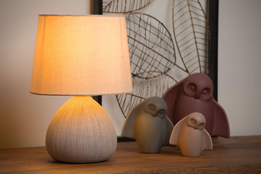 Détail rapproché de la lampe allumée, base en coton tissé et chouettes posées sur bois.