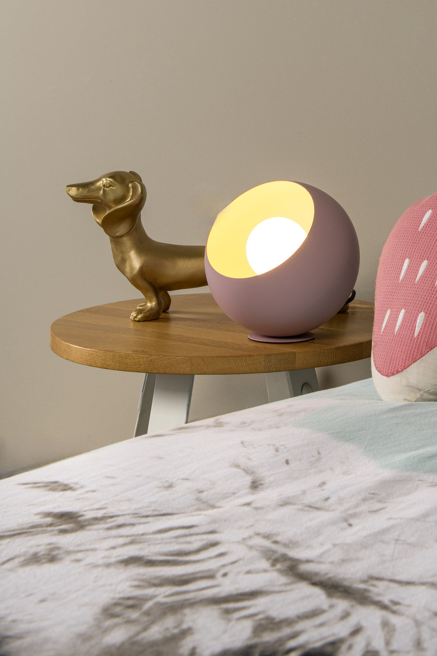 Lampe rose allumée posée sur une table de chevet, près d'une statuette de chien.